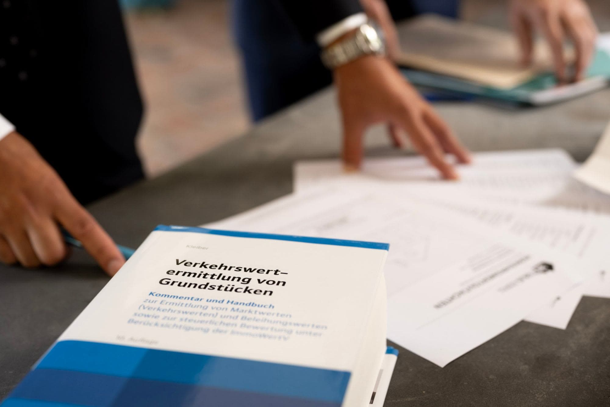 Standardkommentar zur Verkehrswertermittlung von Grundstücken auf dem Arbeitstisch, daneben Gutachtenseiten in der Durchsicht